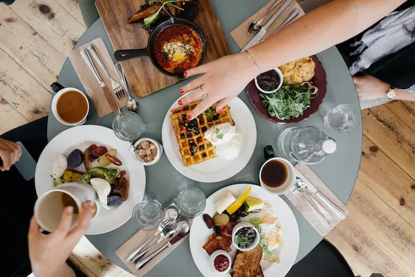 Top view of multiple breakfast dishes on a small table with people around it.