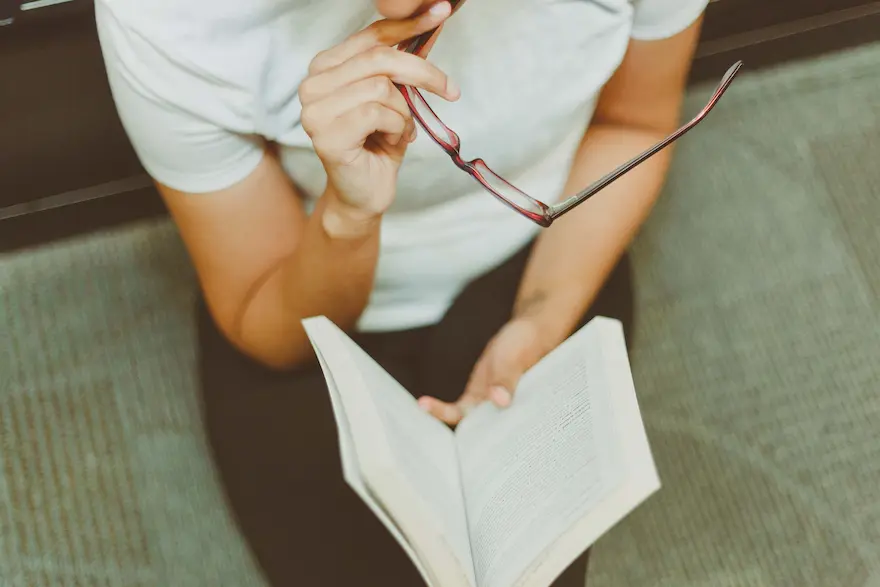 Shot looking down on a person holding a book and pair of glasses